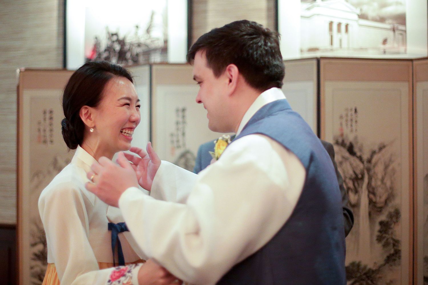 Two people share a joyful moment together in front of a decorative Asian screen displaying traditional artwork.