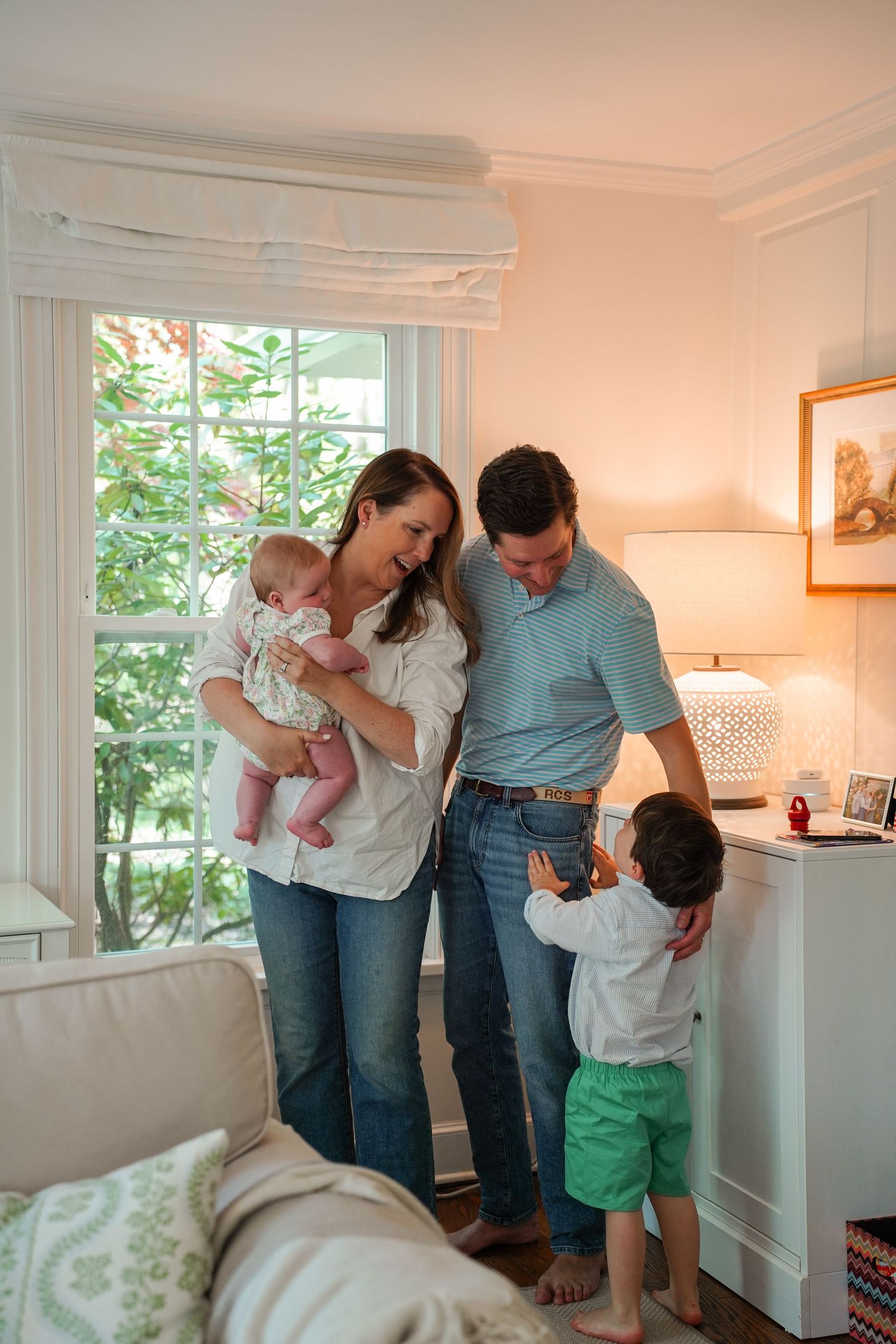 Family spending time together in a cozy corner of their home with a warm lamp light and window view.