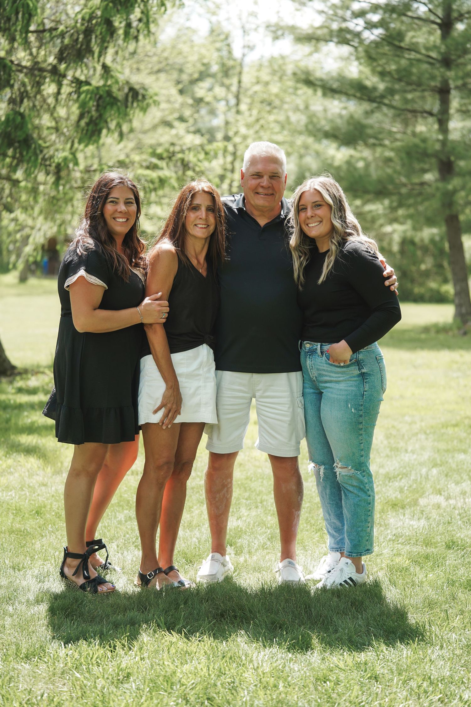 A group poses together outdoors on a sunny day with trees and greenery in the background.