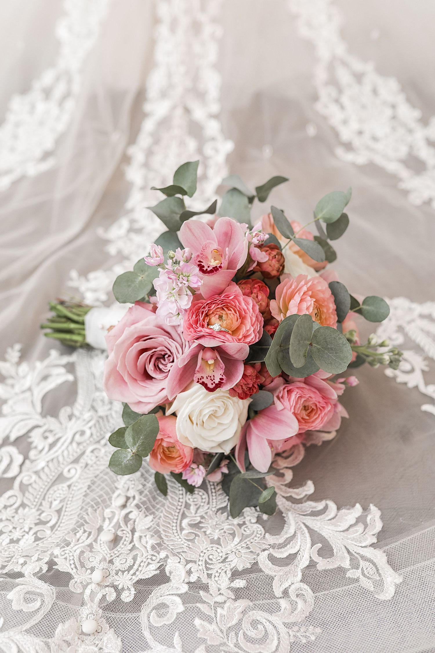 Beautiful bridal bouquet with pink and coral roses, white flowers and eucalyptus leaves resting on delicate lace fabric.