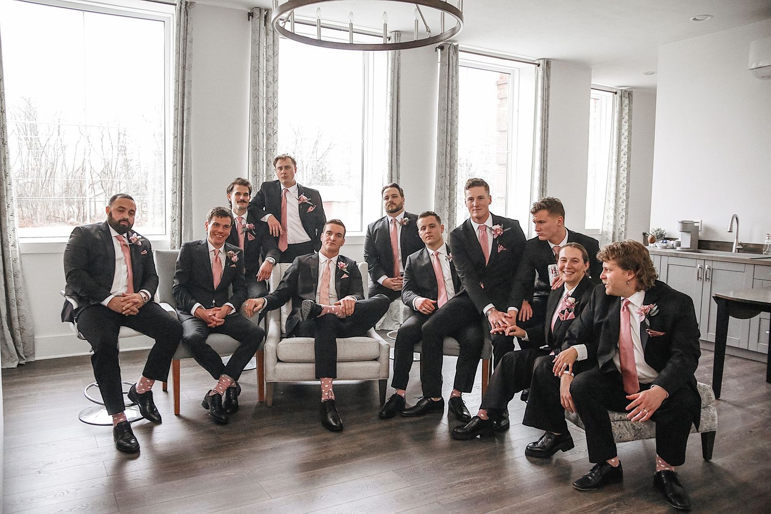 A creative wedding party poses together in formal attire while crouching in a line along a bright indoor hallway.