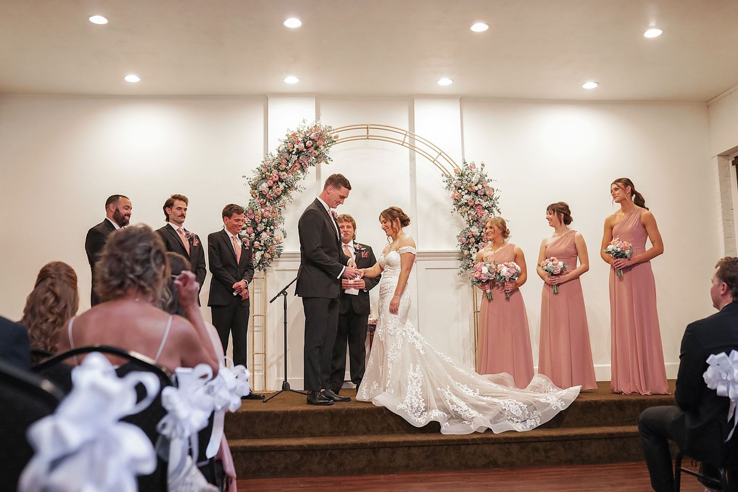 Wedding party members gather on stage in a church sanctuary with pink and white decor for formal ceremony photos.