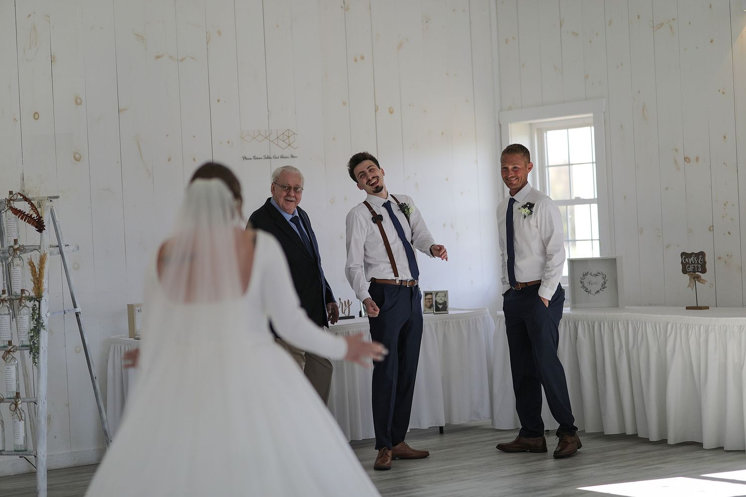 Bridal party and wedding guests gathered in a bright white industrial venue during a wedding celebration.