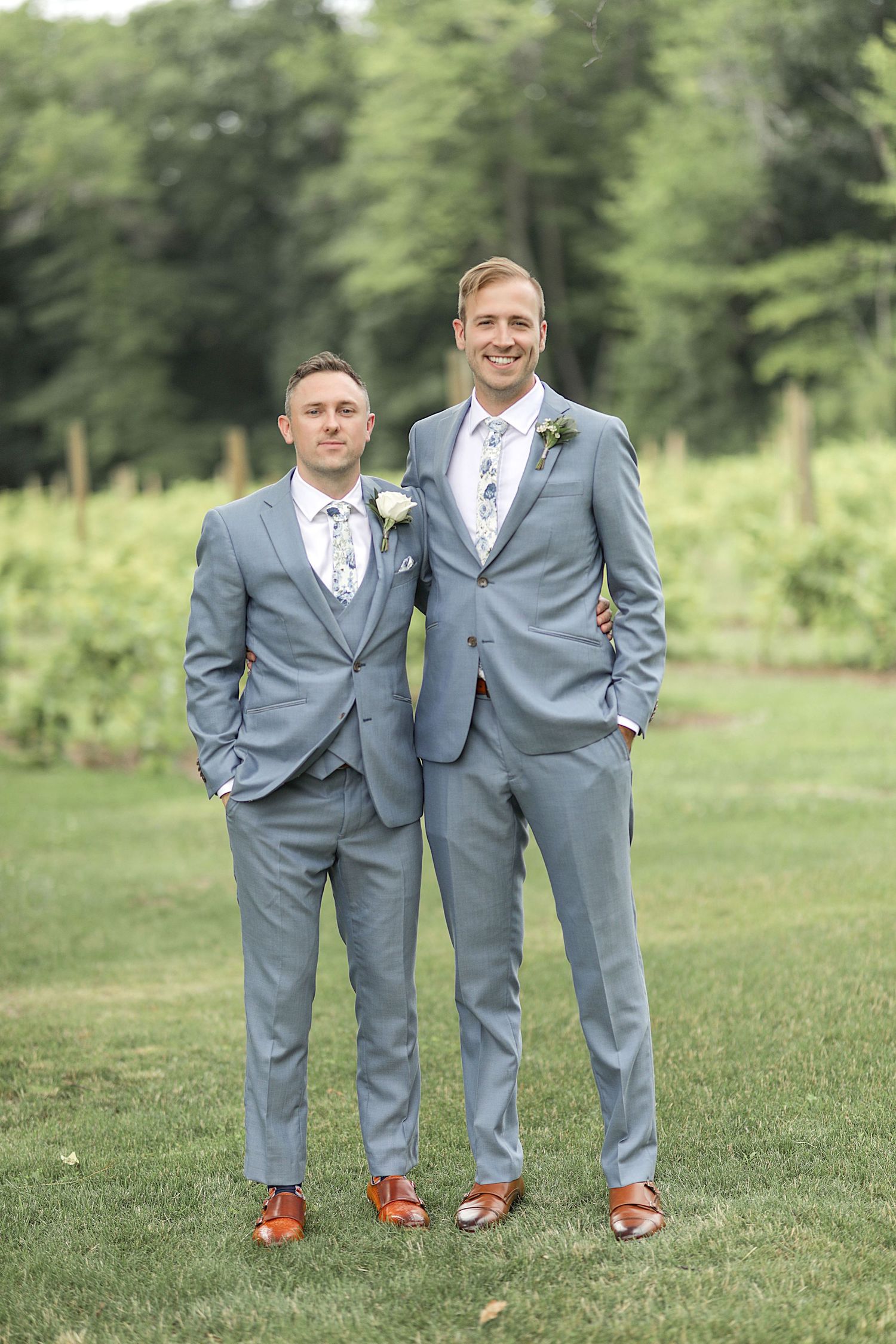 Wedding party members in coordinating gray suits pose for a formal portrait on grass.