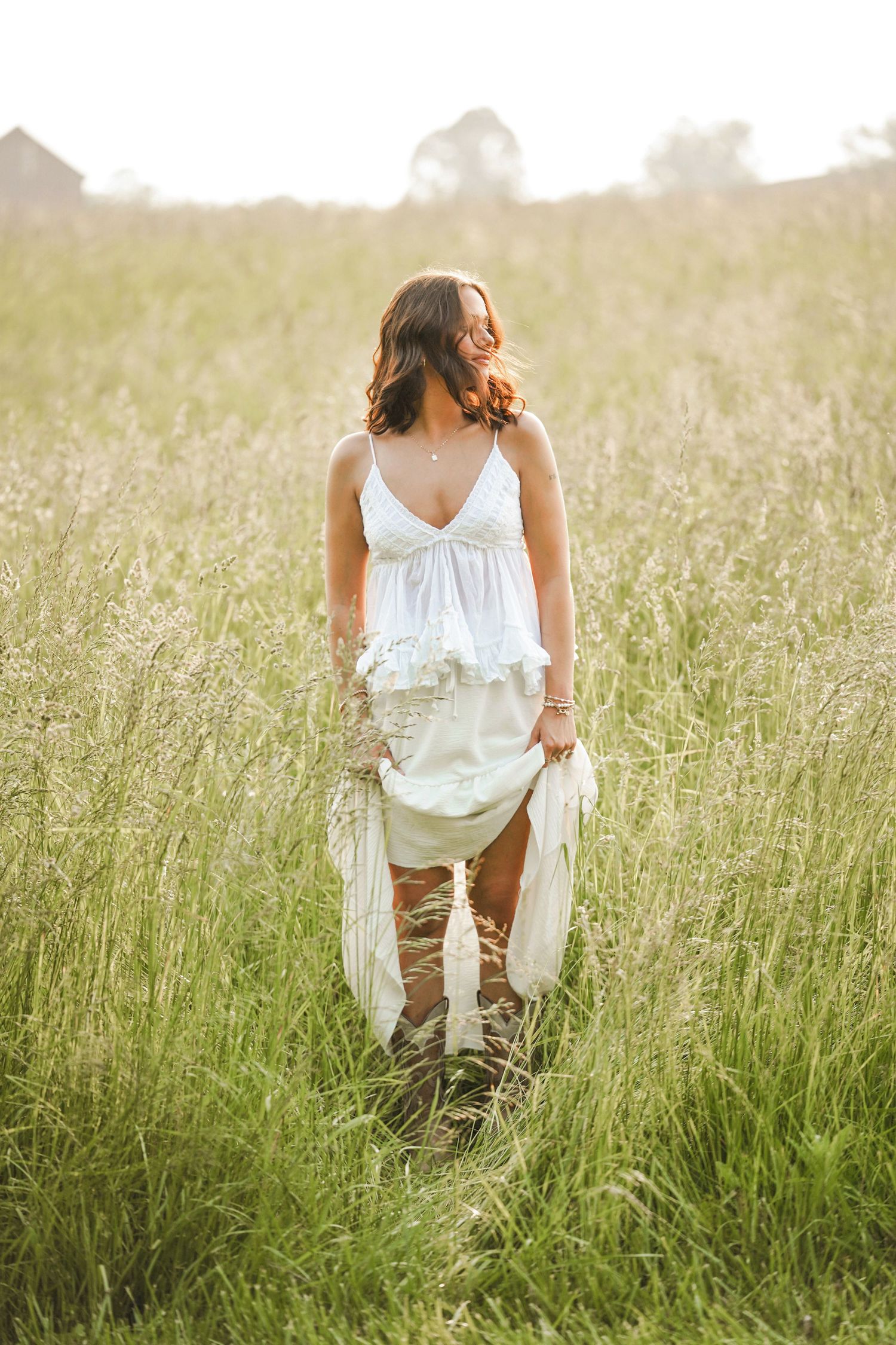 A person wearing a white top and khaki pants crouches in tall sunlit grass during golden hour.