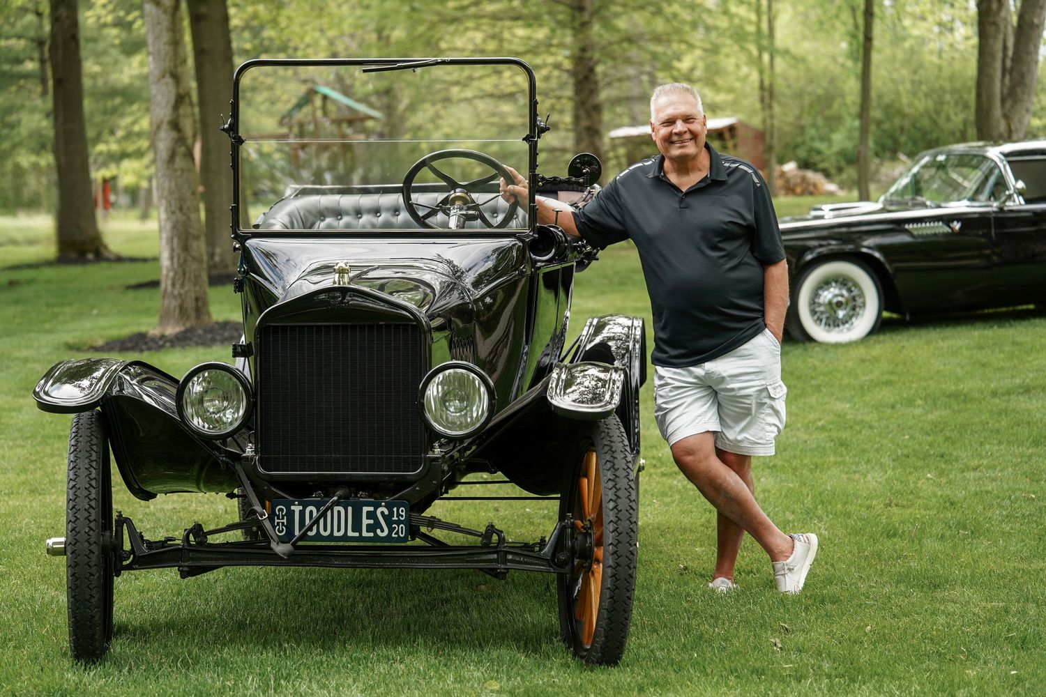 A vintage black Model T Ford automobile displayed on grass with trees in the background.