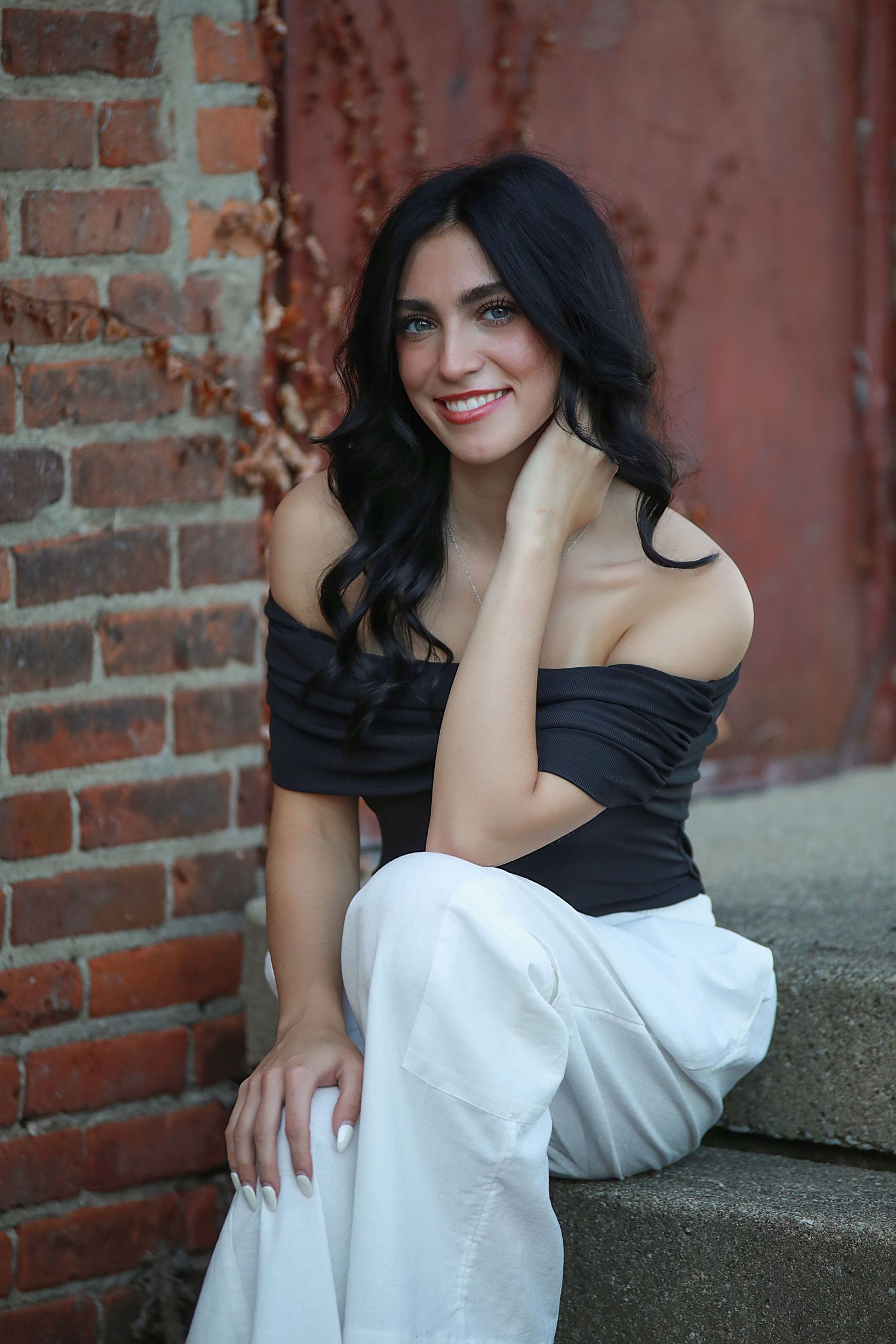 Senior photography in Brecksville, Ohio. A fashion portrait against brick wall wearing black off-shoulder top and white pants.