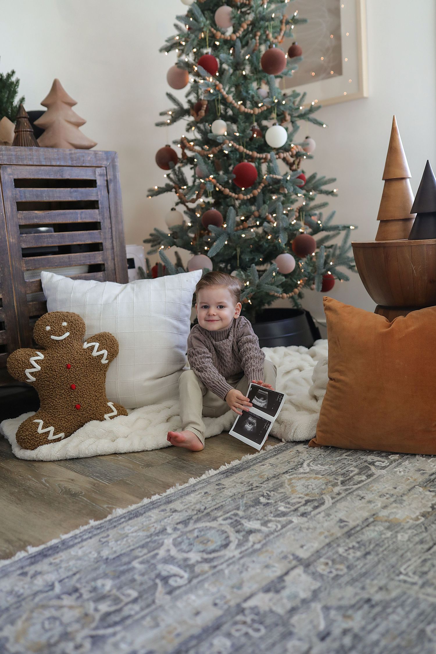 Cozy holiday scene with decorated Christmas tree, gingerbread pillows, and ornate area rug in a modern rustic setting.