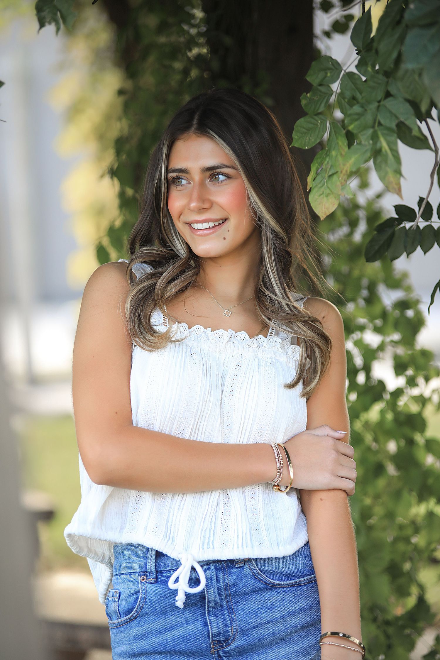 A series of portrait photos showing someone wearing a white ruffled top and denim in a garden setting with green foliage.