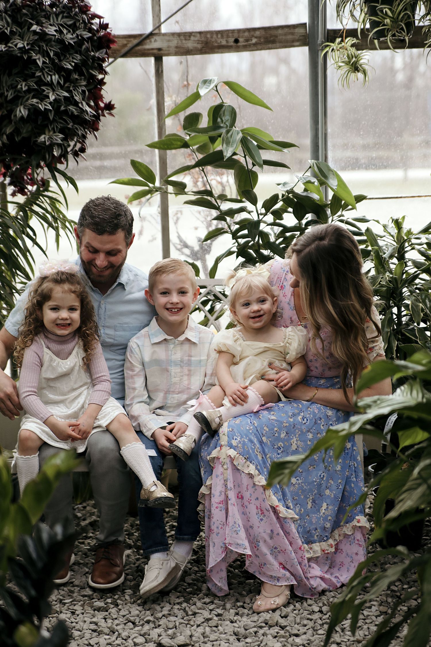 A family shares joyful moments together while sitting on a decorative stone ledge in a greenhouse with lush plants.