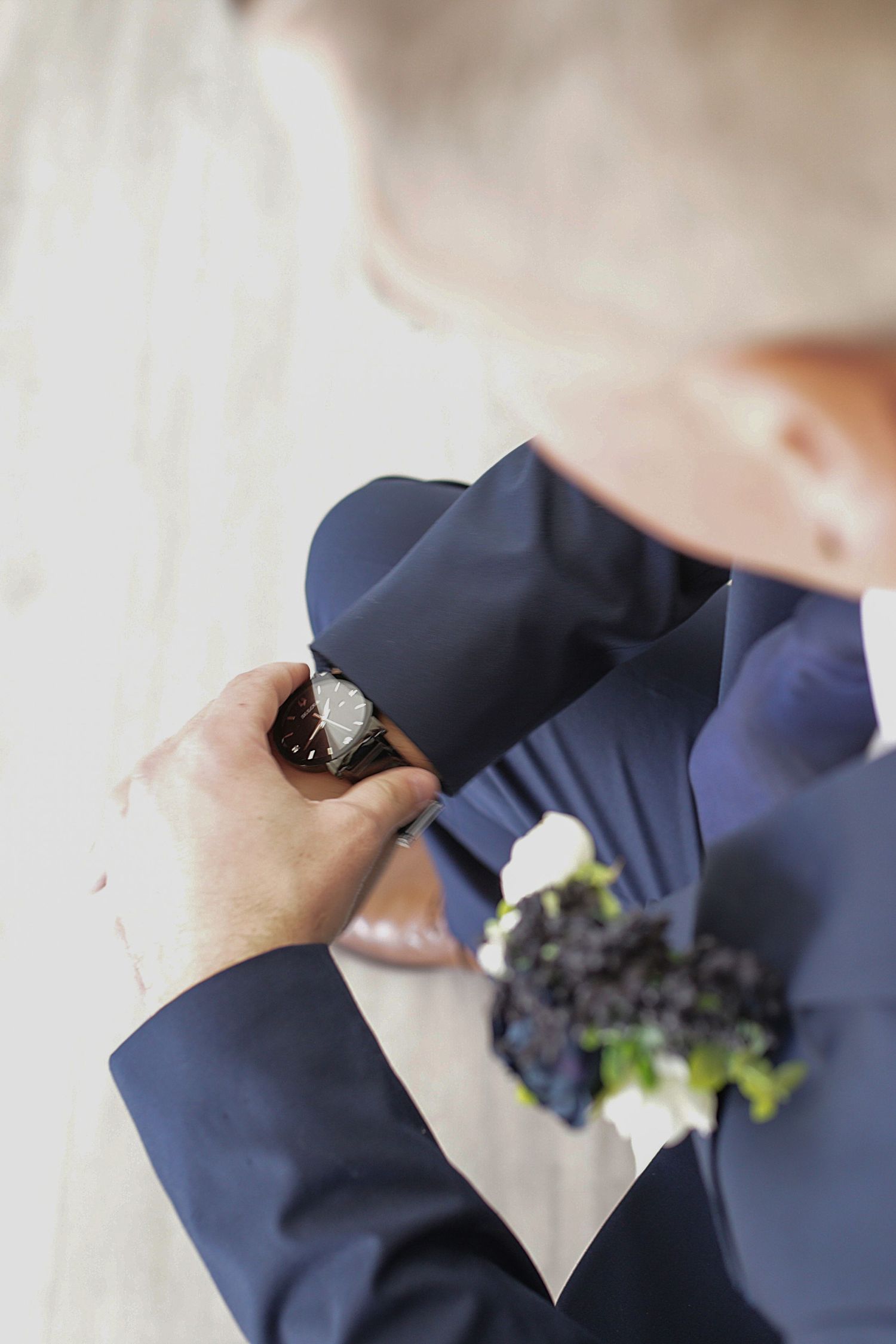 Close-up shot of hands pinning a white boutonniere onto a navy blue suit jacket.