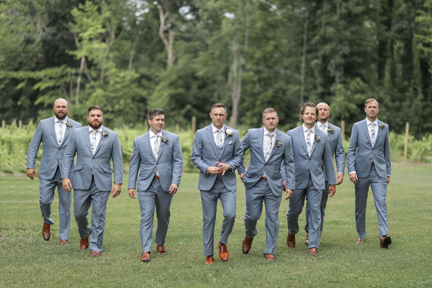 Group of groomsmen in matching light blue suits walking together across grass. Cleveland wedding photographer.