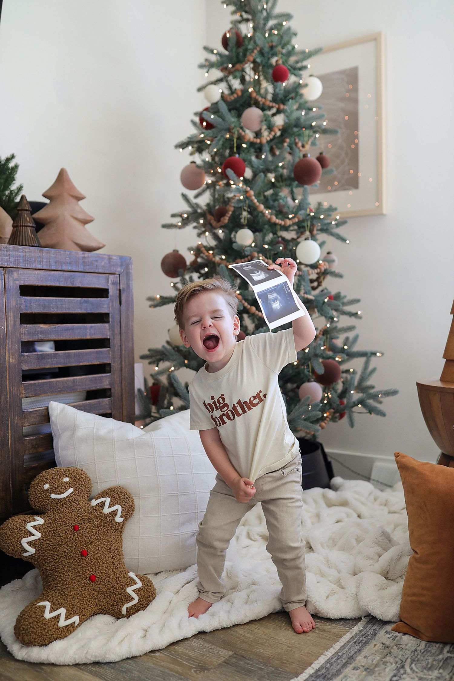 Decorated Christmas tree stands by wooden crate with gingerbread pillow and holiday decor creating festive scene.