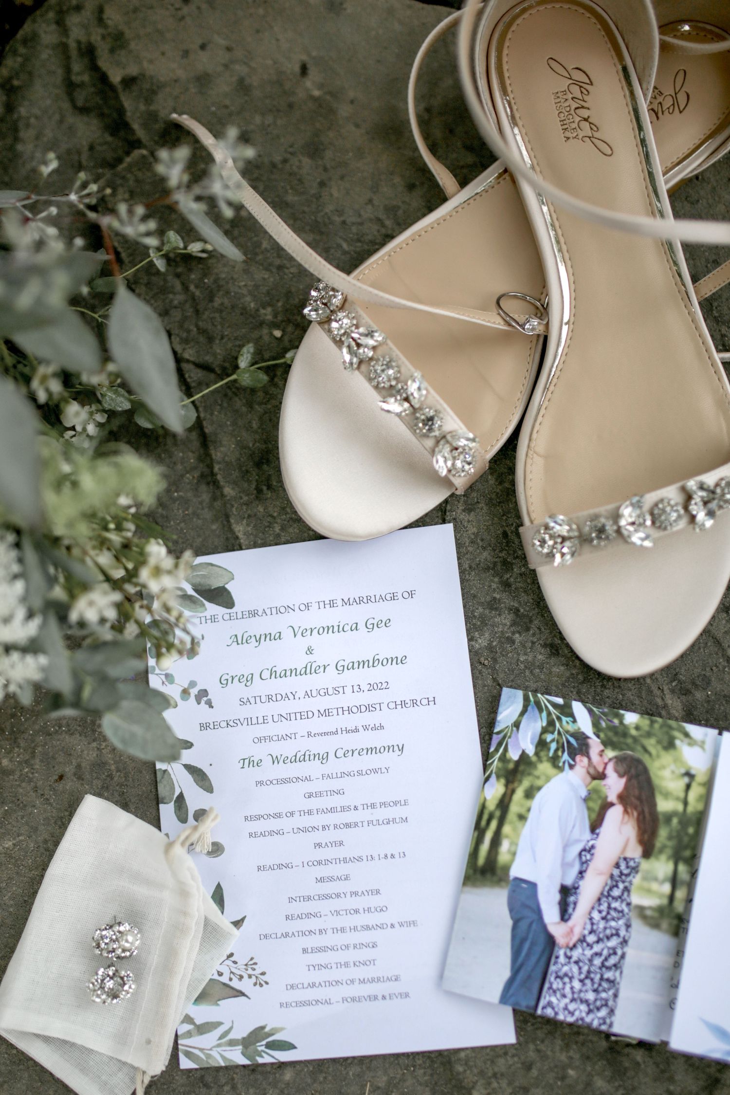 Wedding invitation suite with sparkly bridal shoes and delicate floral details laid out on a textured stone surface.