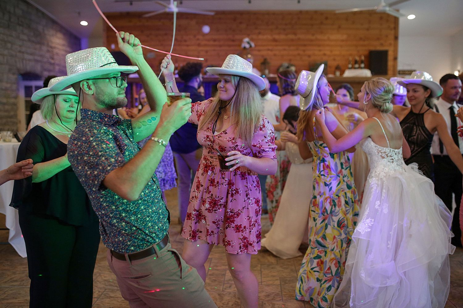Wedding guests dancing in colorful attire under purple lighting at an indoor reception venue.