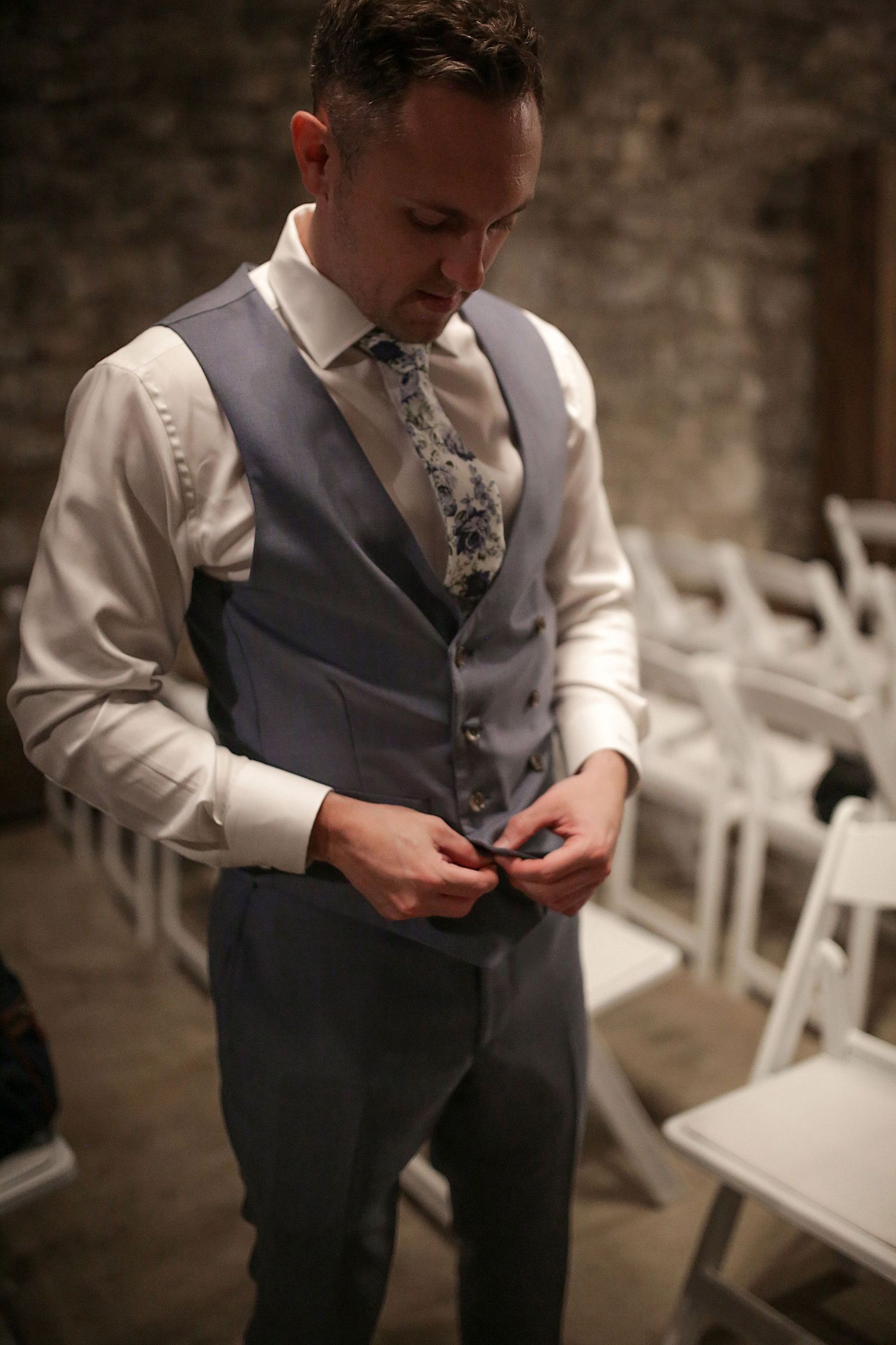 Wedding preparations show groom adjusting cufflinks near white ceremony chairs.