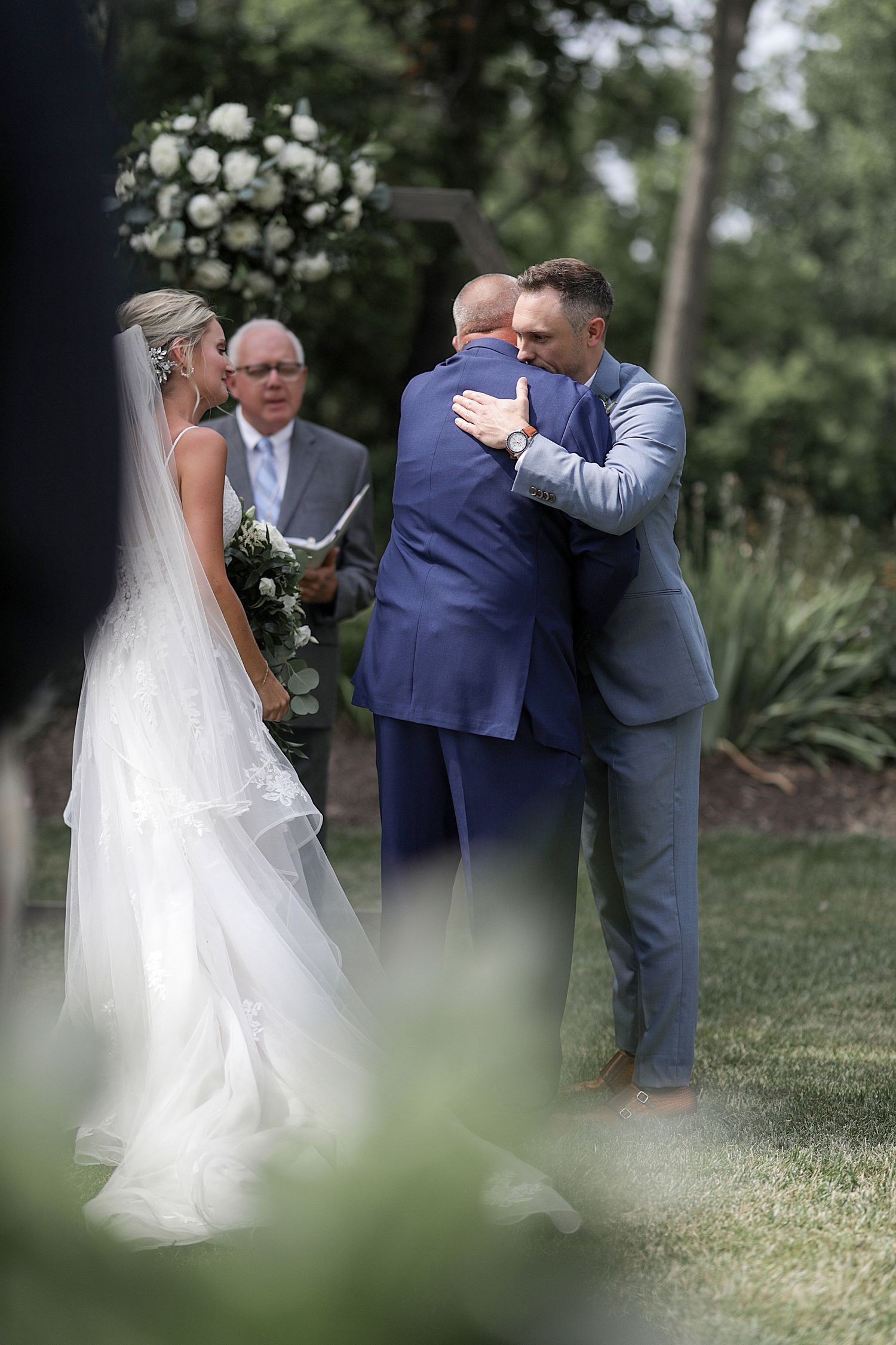 Romantic outdoor wedding ceremony on a grassy lawn with trees in the background.