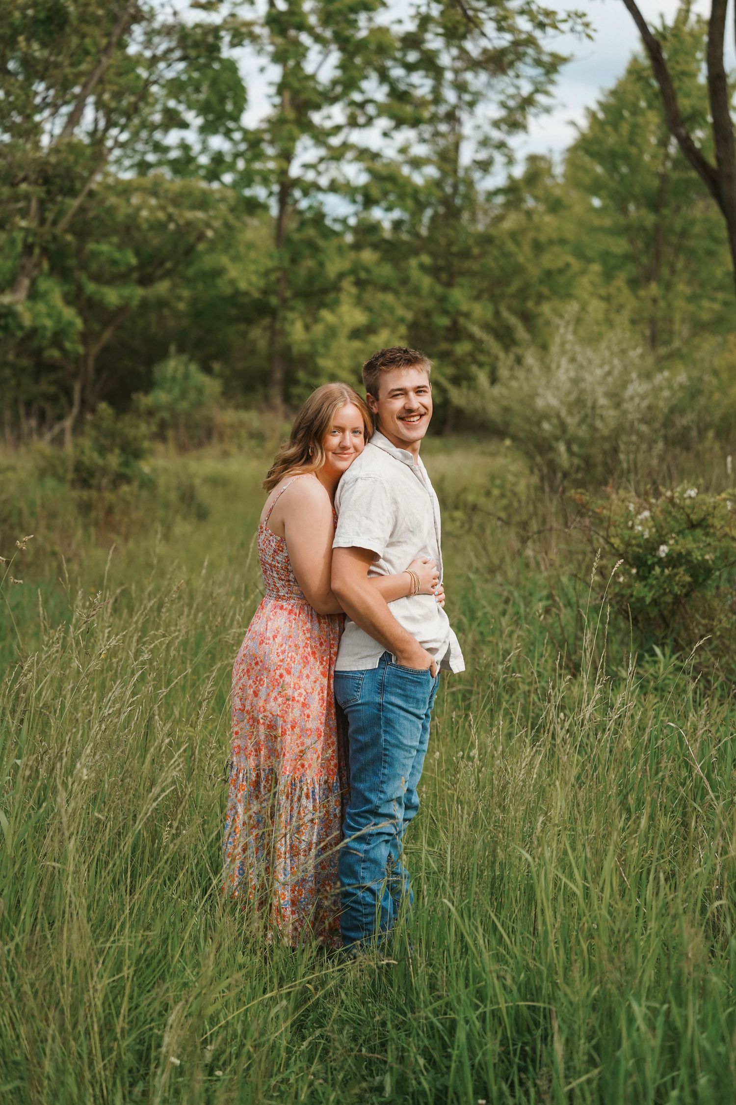 Two people embrace tenderly in a field of tall summer grass on a sunny afternoon.
