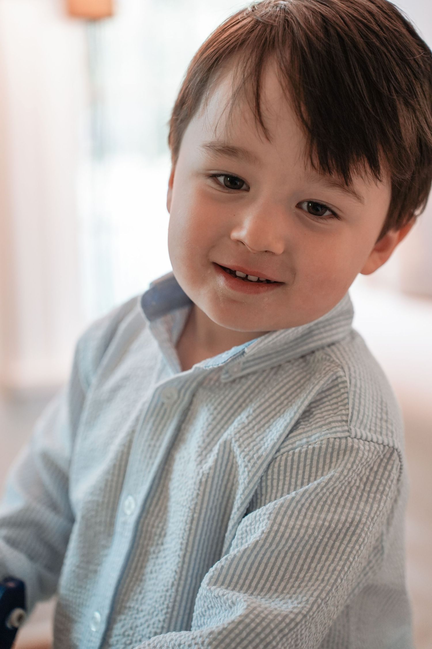 Adorable toddler in light gray sweater smiling and posing for photos in a bright indoor setting.