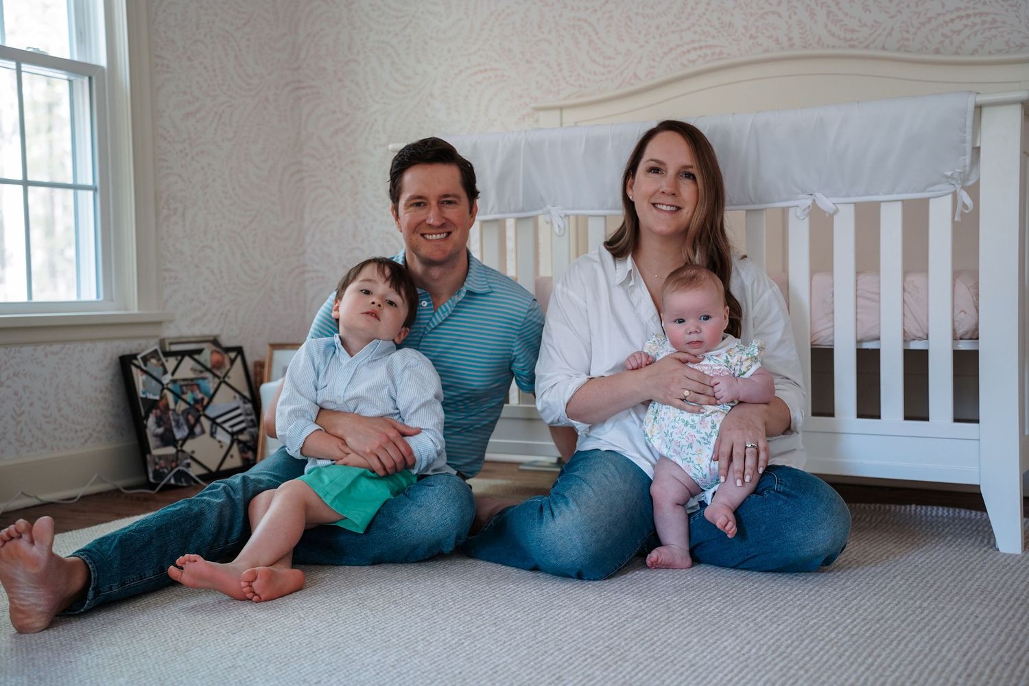 Family members sitting on floor together wearing jeans and casual tops in white room interior.