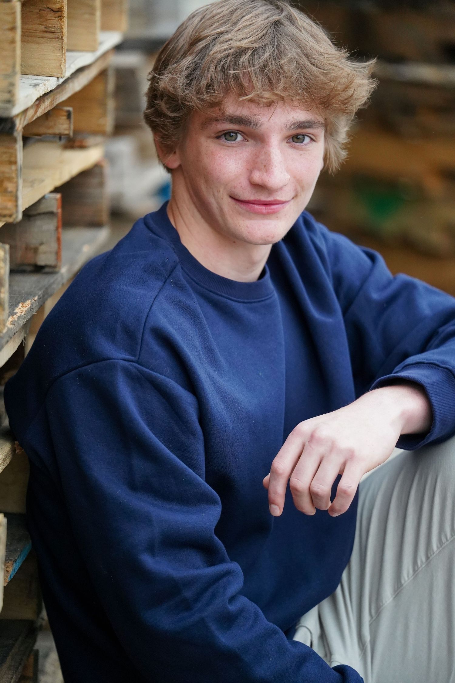Person wearing navy blue sweatshirt sits casually against light colored furniture in wooden room setting.