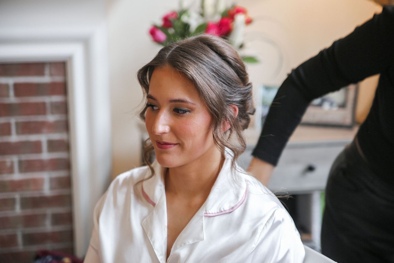 Someone wearing a white silk robe sits while getting ready, with a brick wall and pink flowers visible in background.