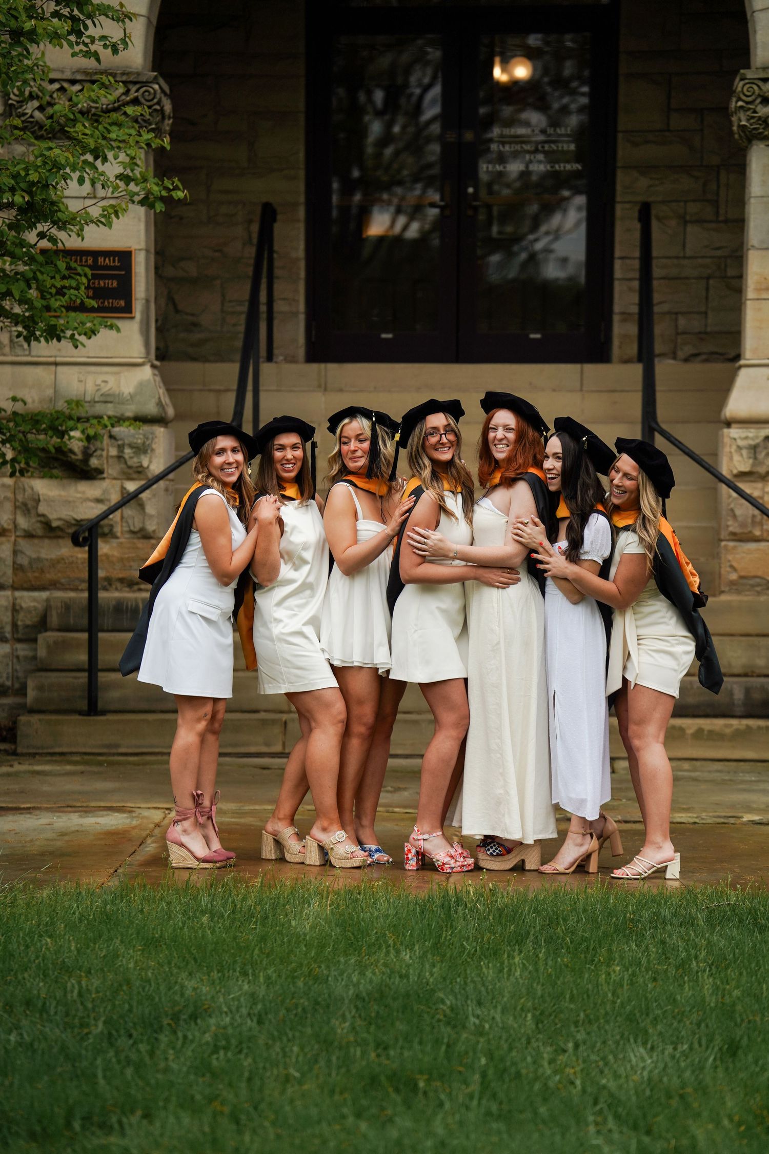 Group of people in white dresses and high heels posing together on stone steps outside a building.