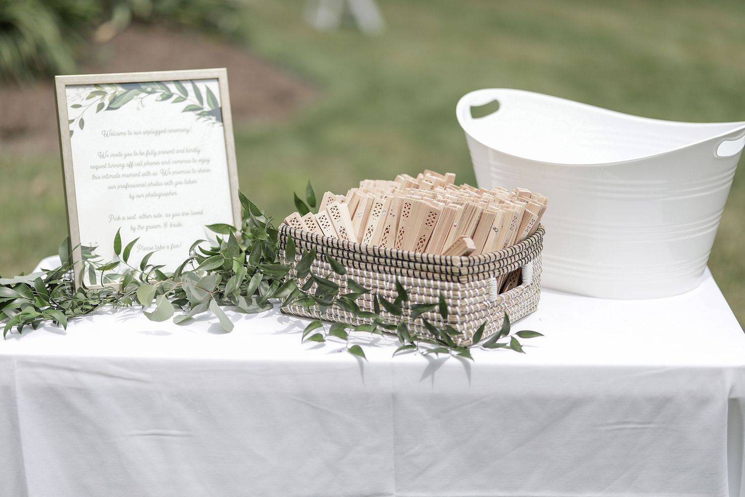 Wedding decorations on white table with greenery and fan favors.