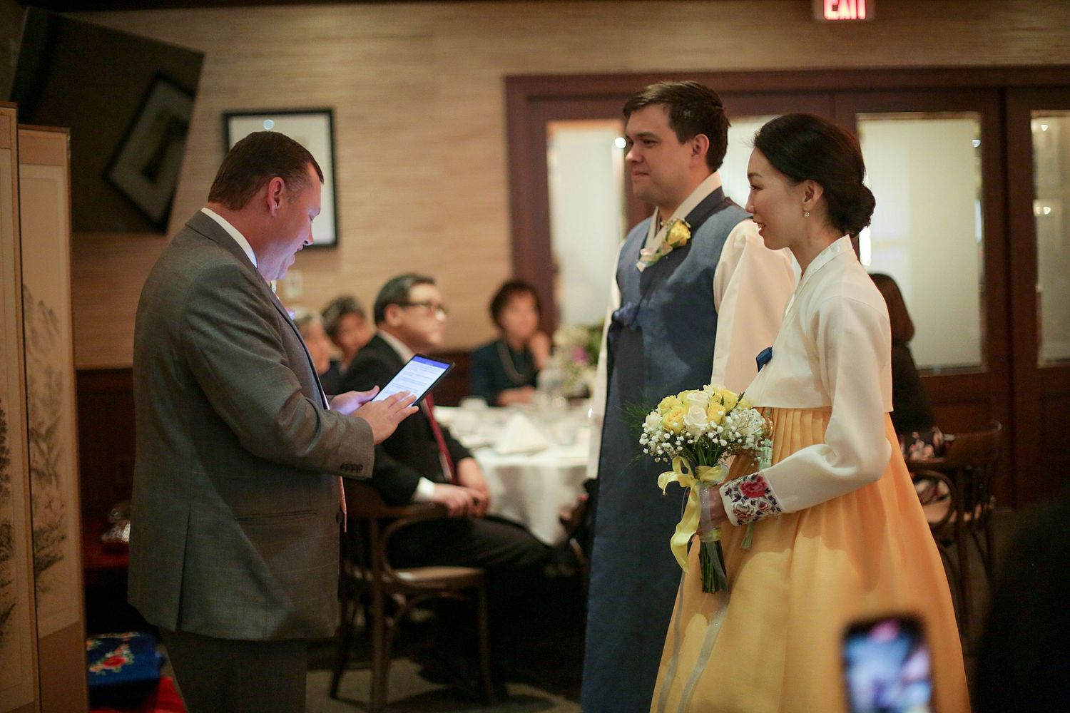 A couple shares their first dance together at a wedding reception while guests watch and take photos.
