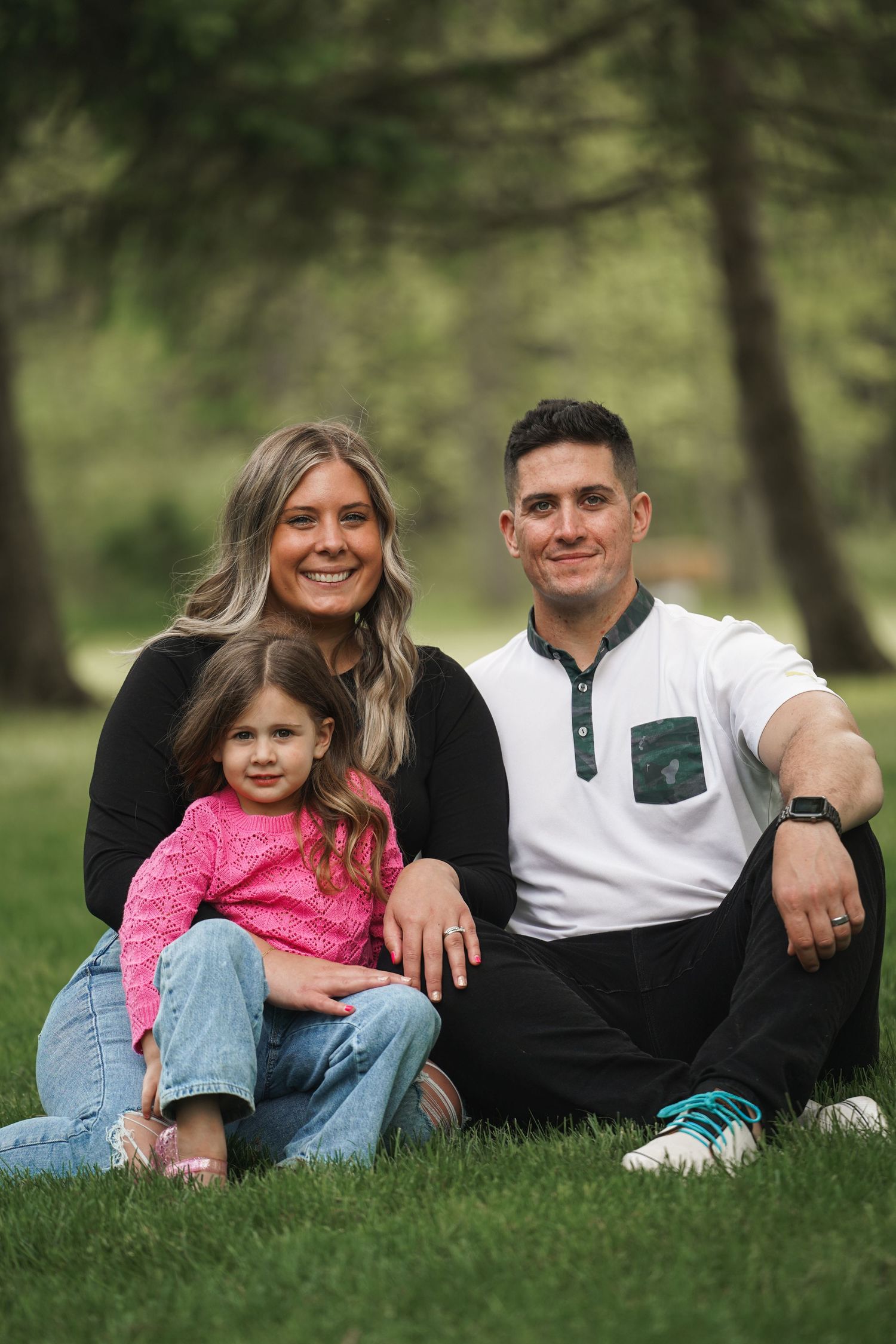 Family sitting together on green grass in a park during a sunny day outdoors.