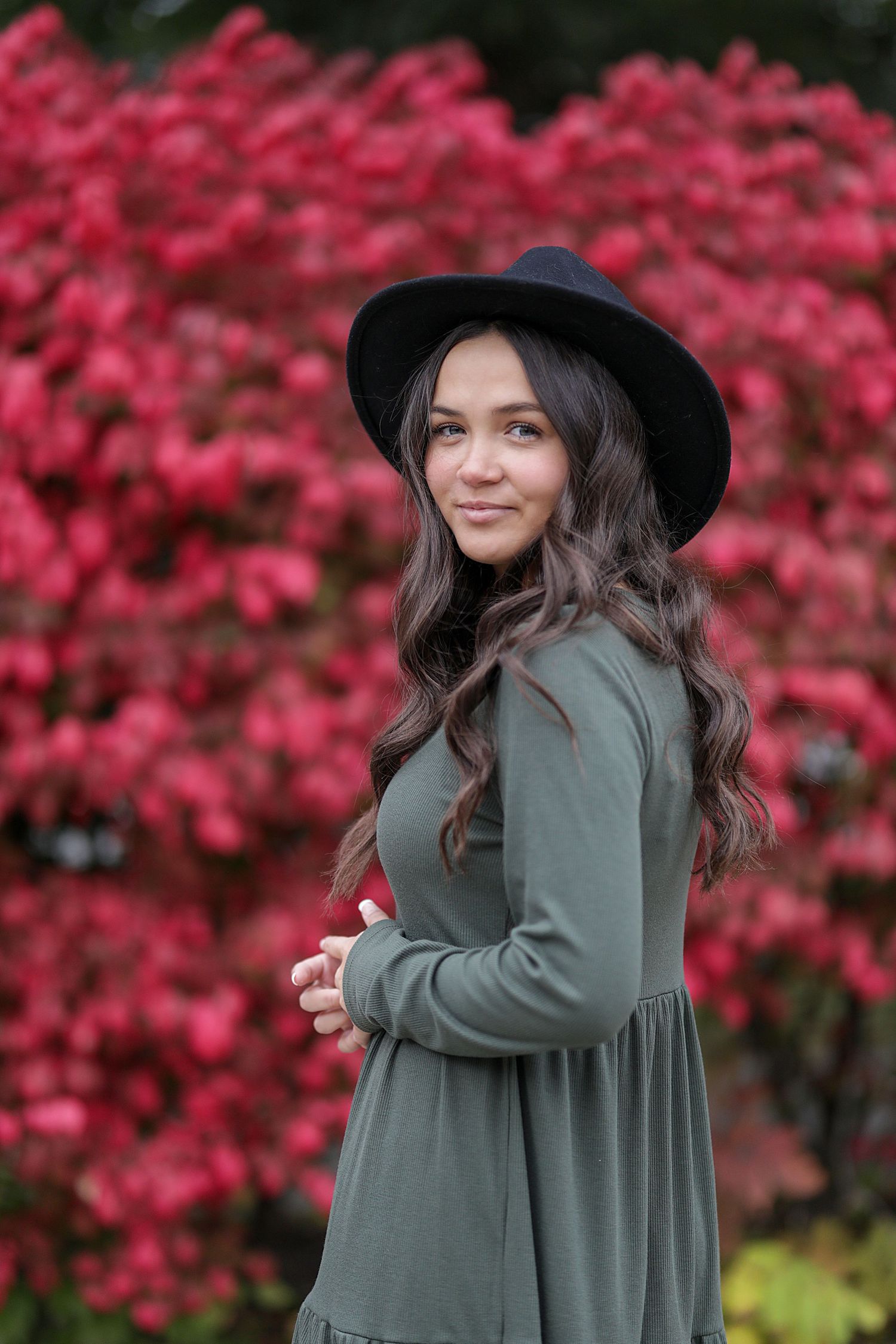 Four sequential photos showing someone posing in a black hat and olive green sweater against vibrant pink fall foliage.