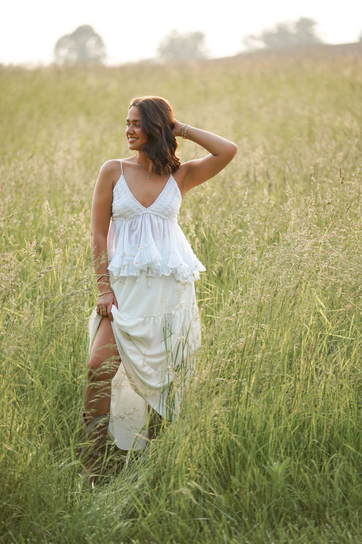 A whimsical fashion photo captures movement in a white dress among tall grass at sunset.
