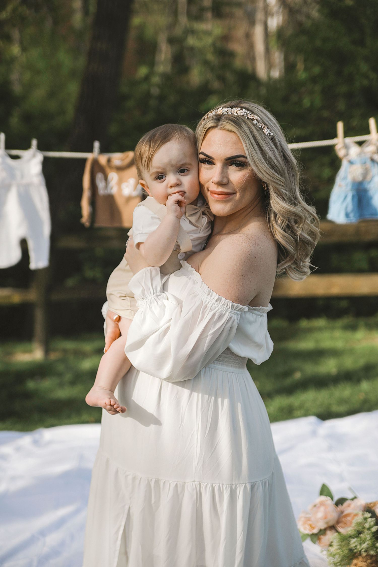 A laundry line outdoors displays white clothing and linens against a green garden backdrop on a sunny day.