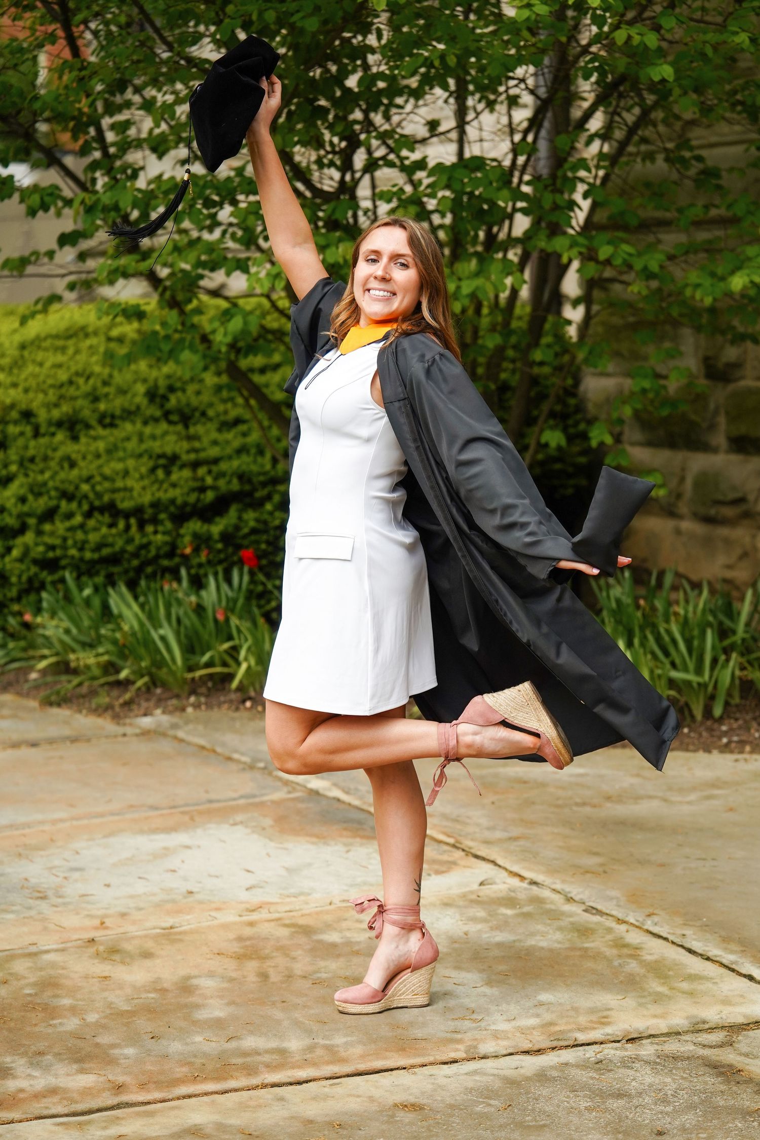 A series of graduation photos showing someone celebrating with a fun leg kick pose in an outdoor garden setting.