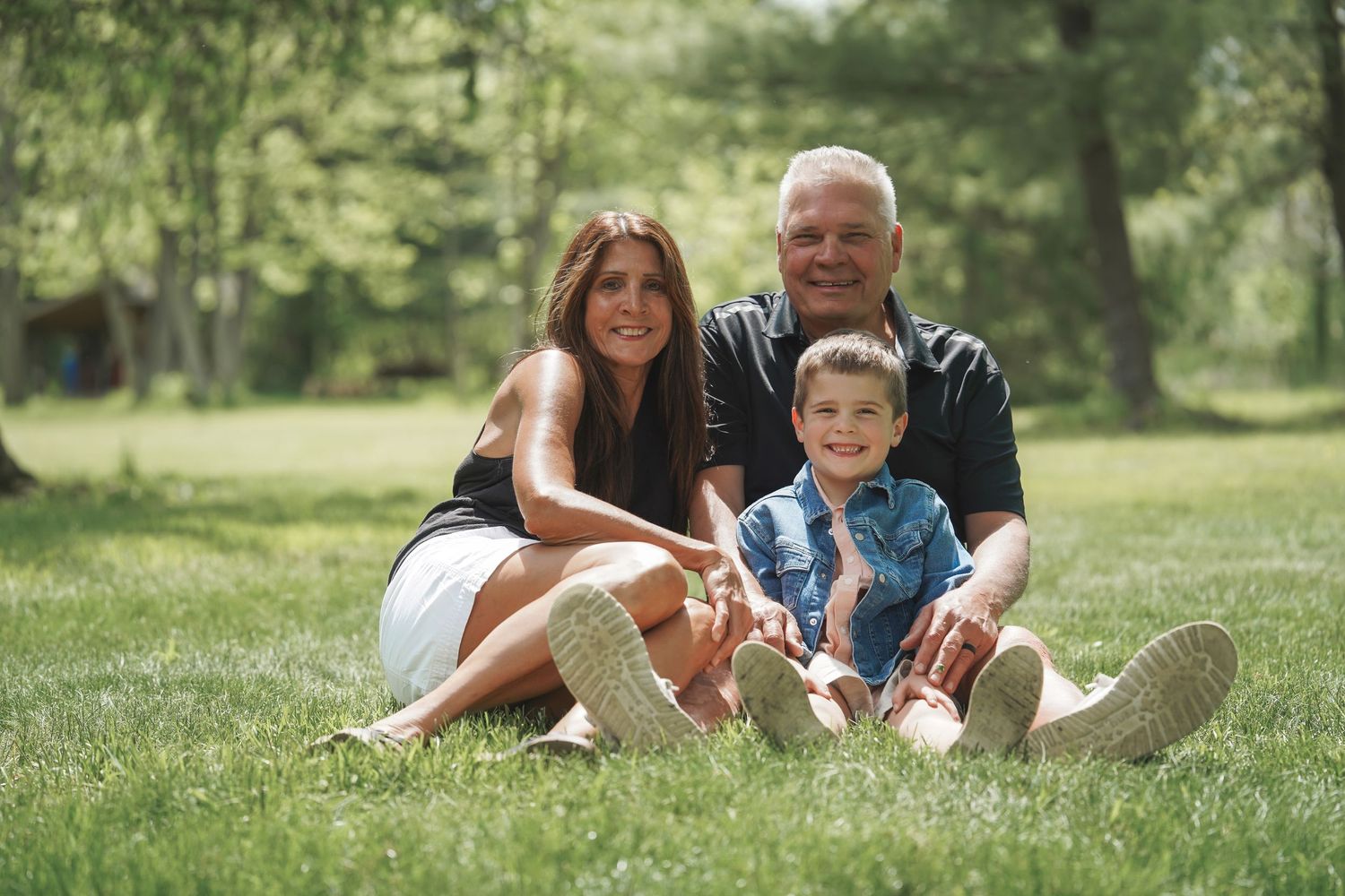 Multi-generational family sitting together on green grass in a sunny park on a summer day.