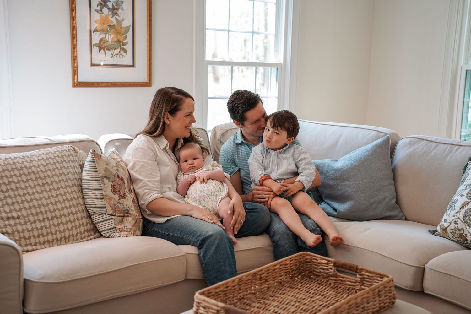 Family relaxing together on white couch in bright living room with art on wall.