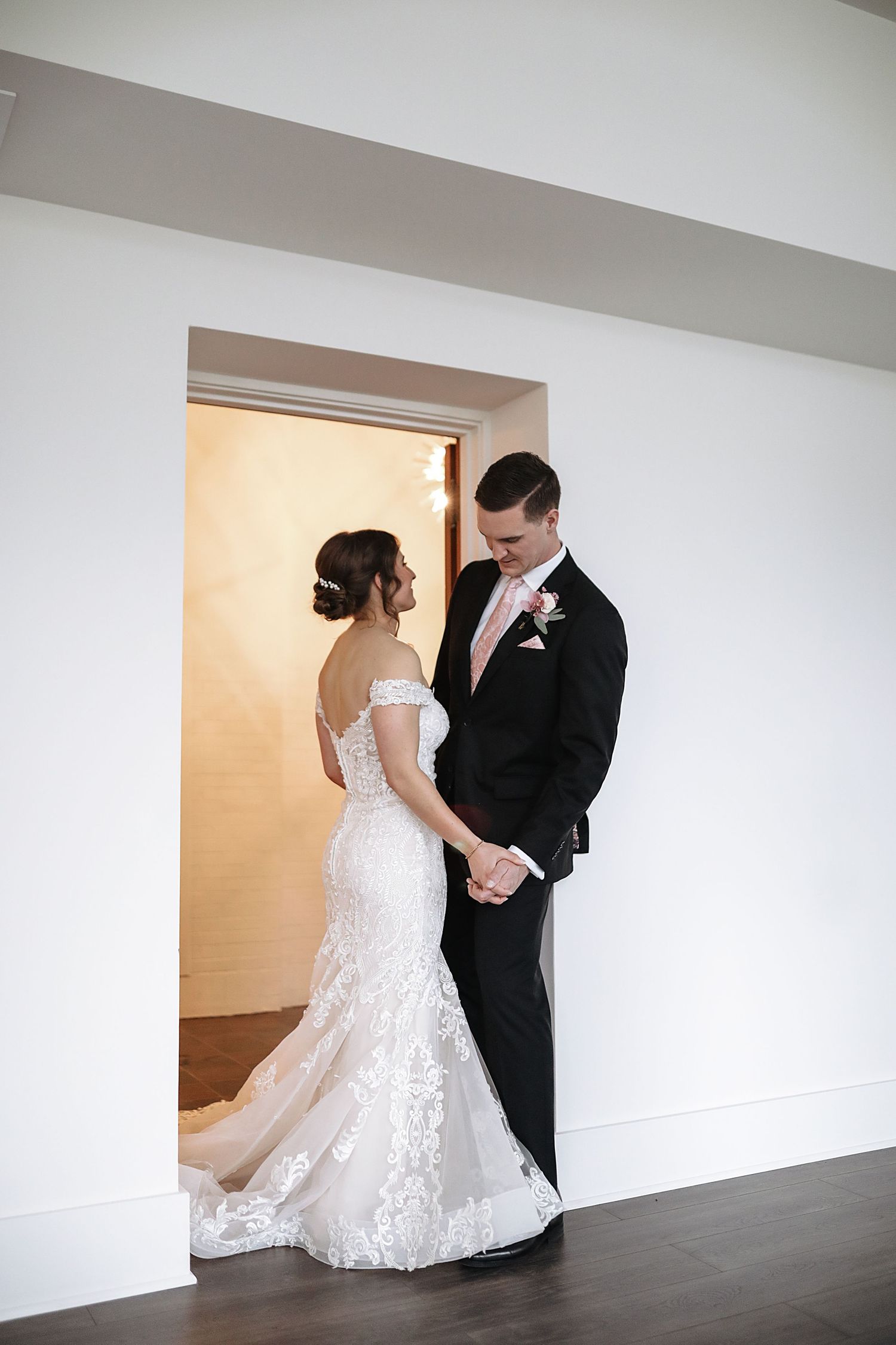 A couple shares an intimate moment in their wedding attire, with the bride wearing a lace mermaid gown and groom in black tuxedo.
