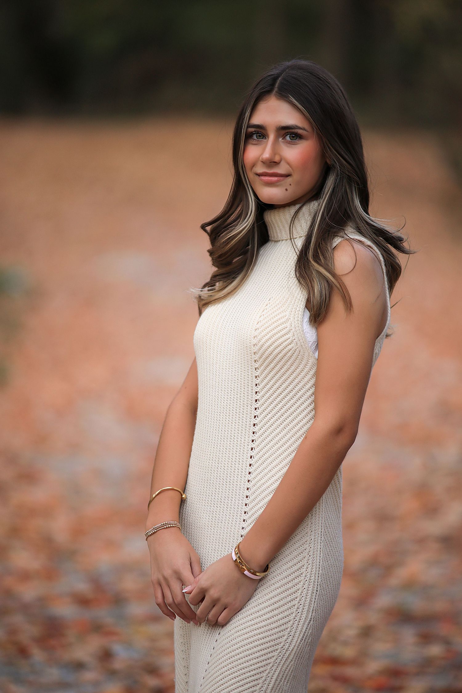 Portrait outdoors on autumn ground showing a person wearing a cream-colored sleeveless knit dress with delicate pattern details.