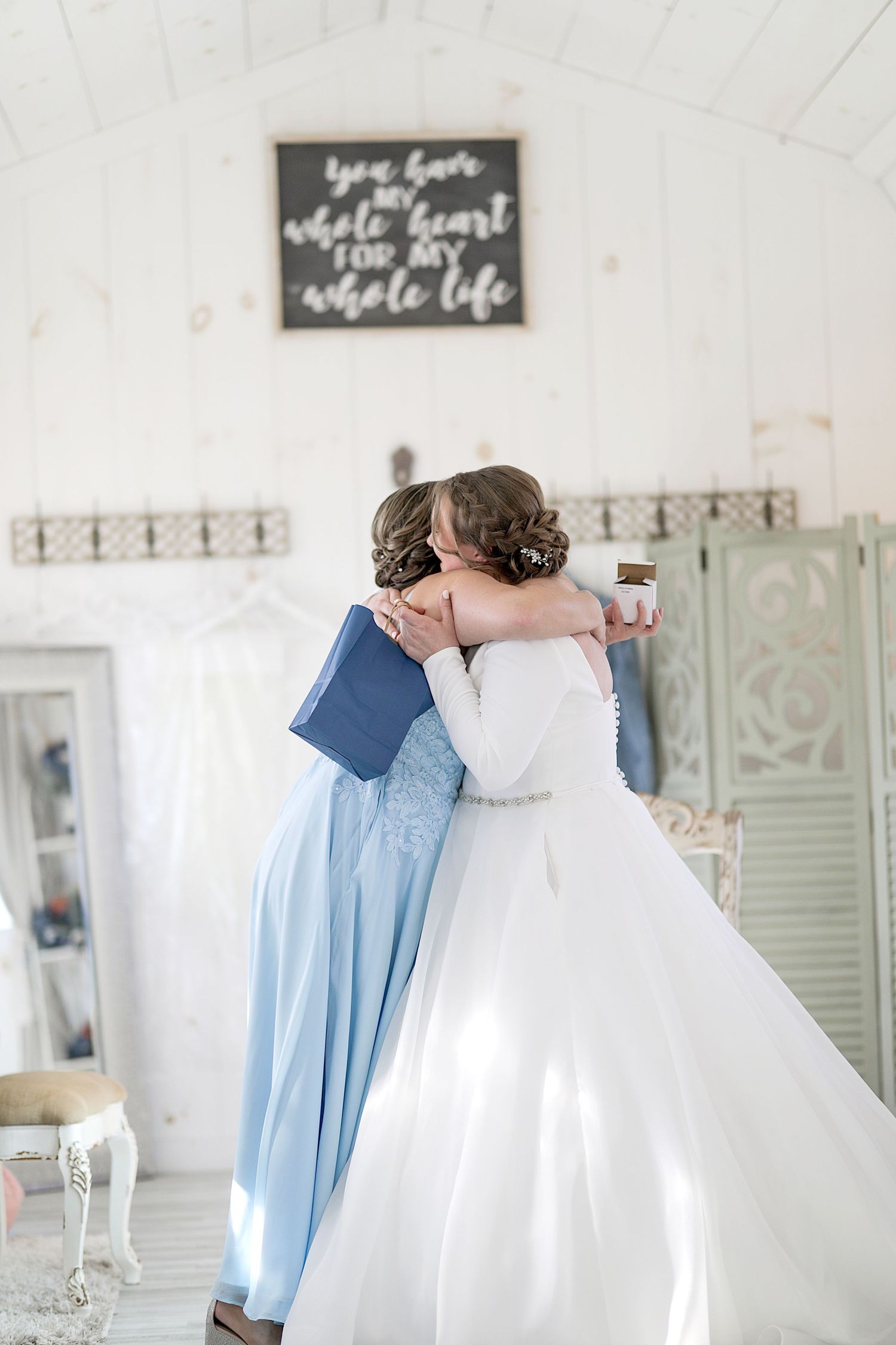 Two people in wedding attire share a tender moment in a white room with decorative signage.