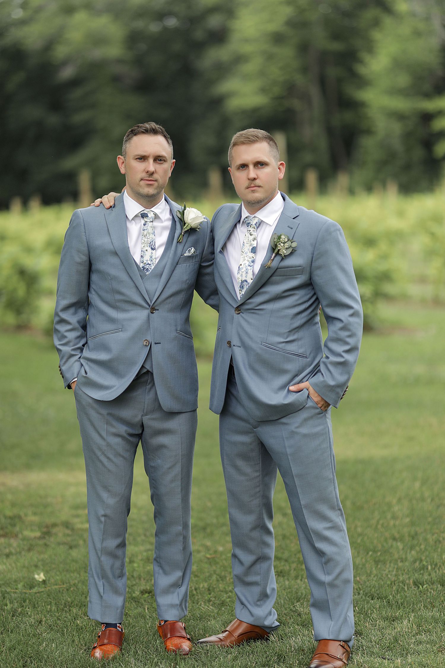 Two men in identical gray suits and floral ties stand together for a formal portrait on a lawn.