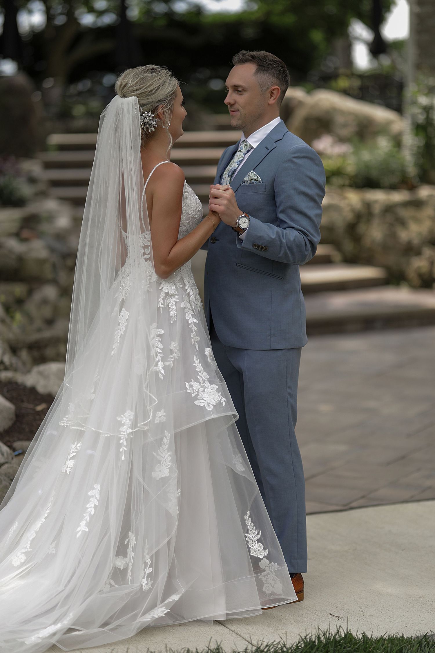 Couple in wedding attire share intimate moment on stone steps outdoors.