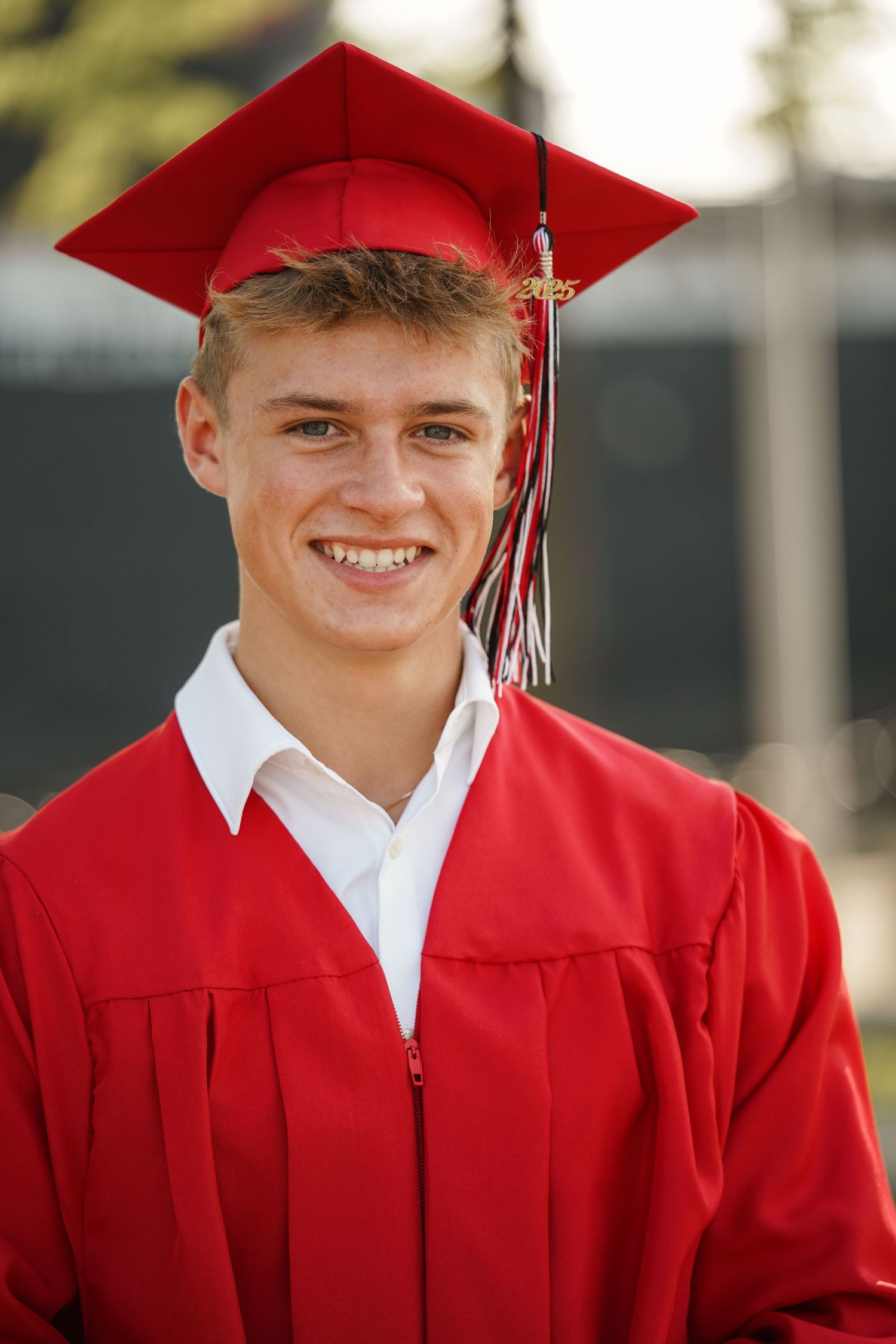 Graduate wearing red cap and gown smiles brightly during commencement ceremony.