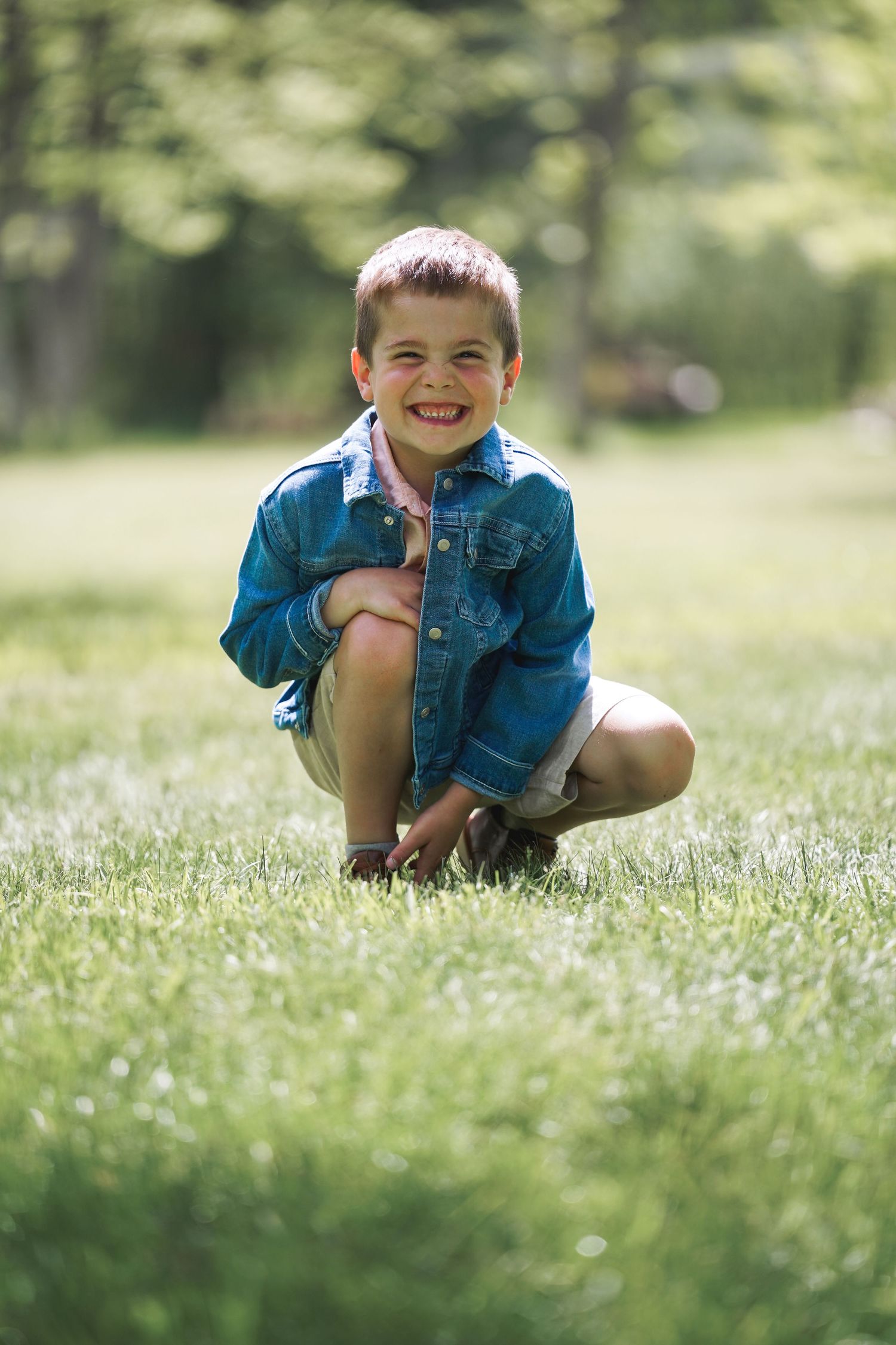 Child in blue denim crouches down while exploring a springtime meadow filled with white wildflowers.
