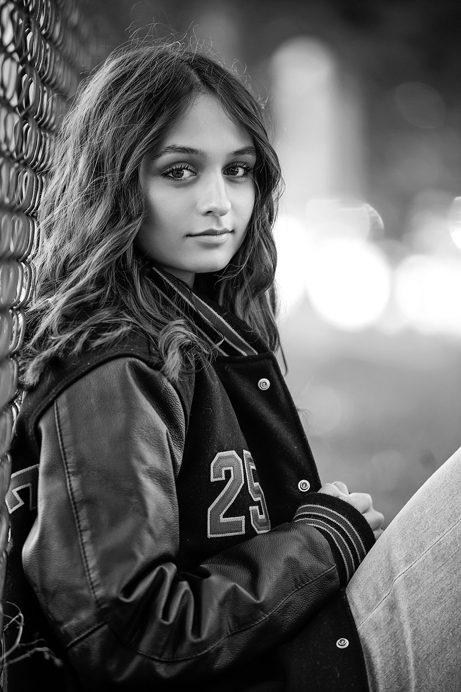 Senior Photography Medina Ohio. A black and white portrait wearing varsity jacket against chain link fence with bokeh background.