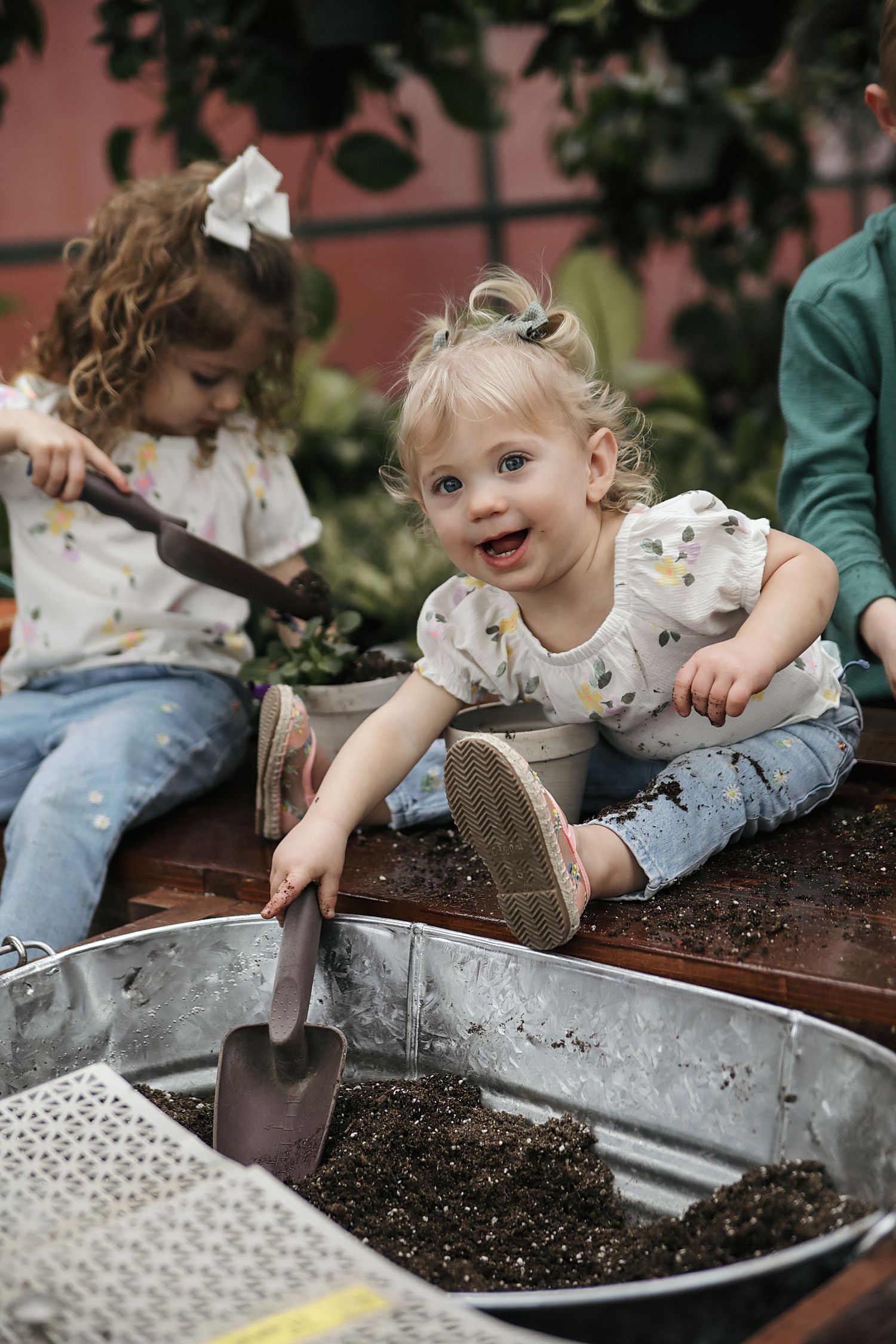 A child plays and explores with soil in a metal container during an outdoor gardening activity.