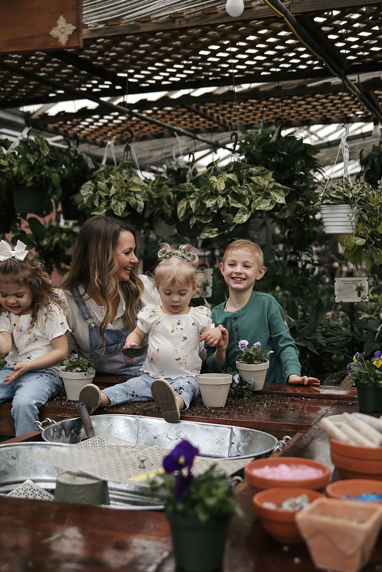 A cozy garden potting session with children gathered around tables filled with plants and terracotta pots.