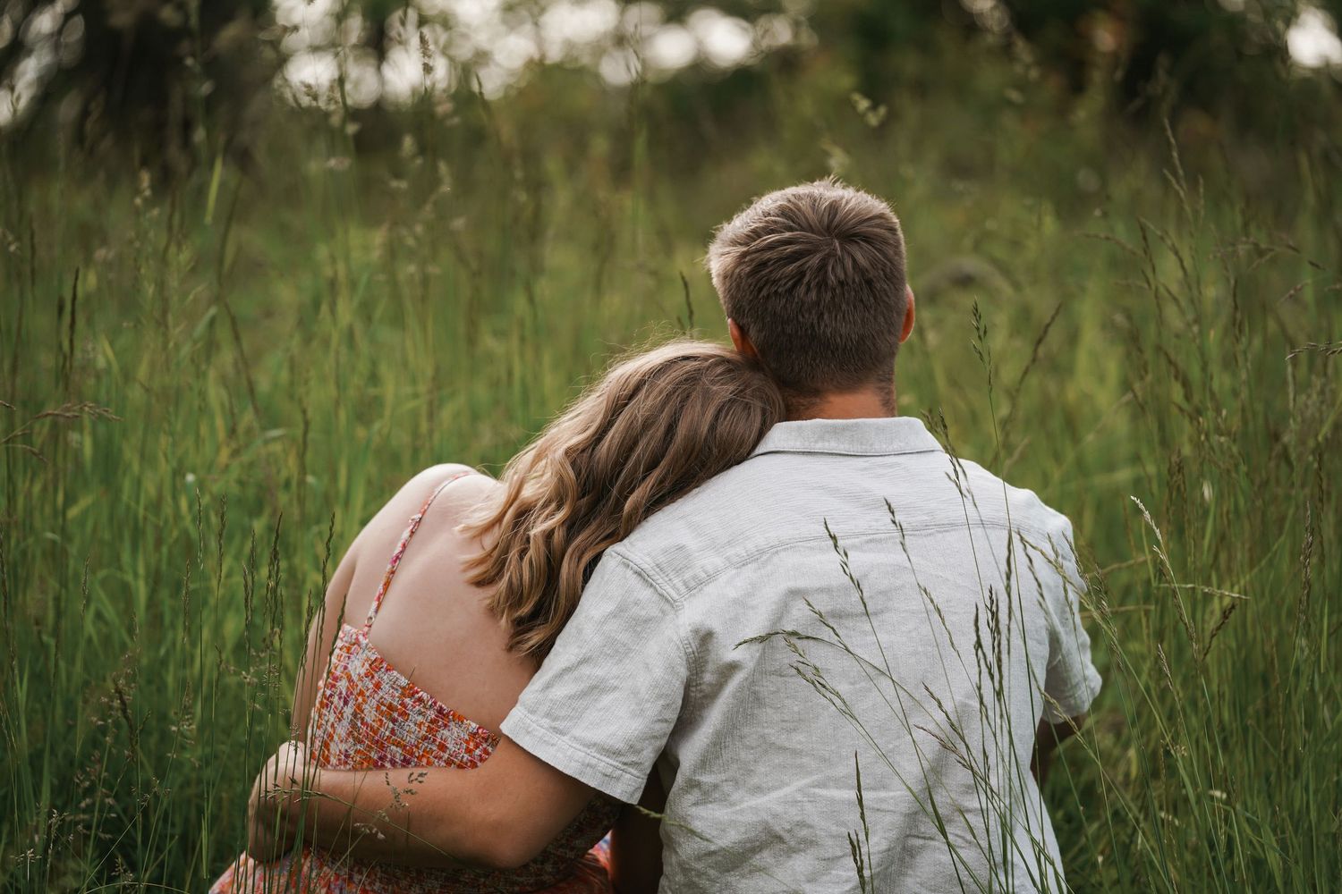 Two people sitting close together in tall green grass on a summer day.