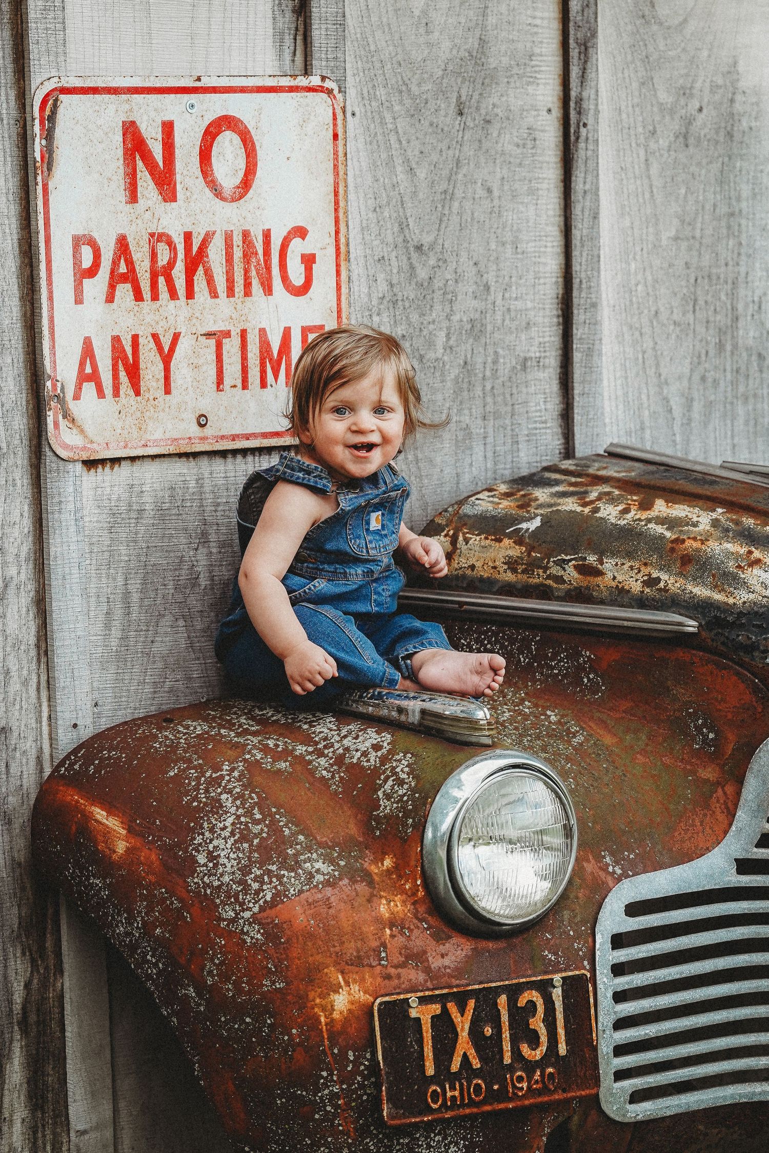 Small children sitting on rusty vintage cars in front of no parking signs.