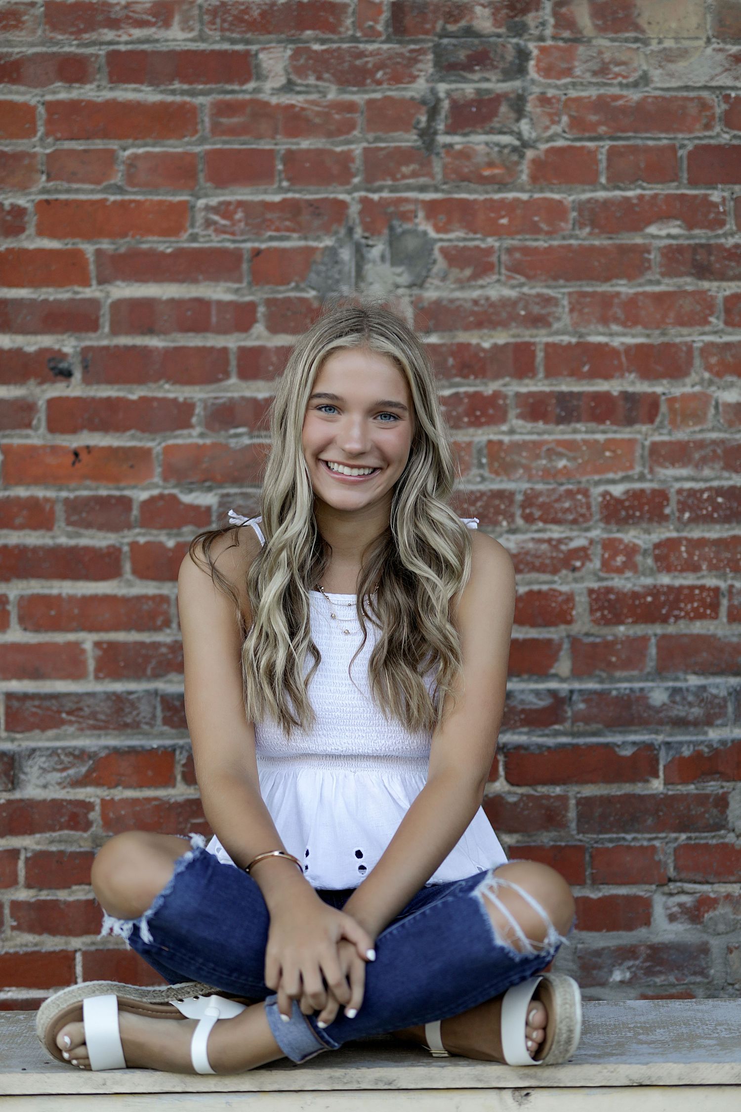 A series of casual portraits taken against a rustic red brick wall with someone sitting wearing white and blue.