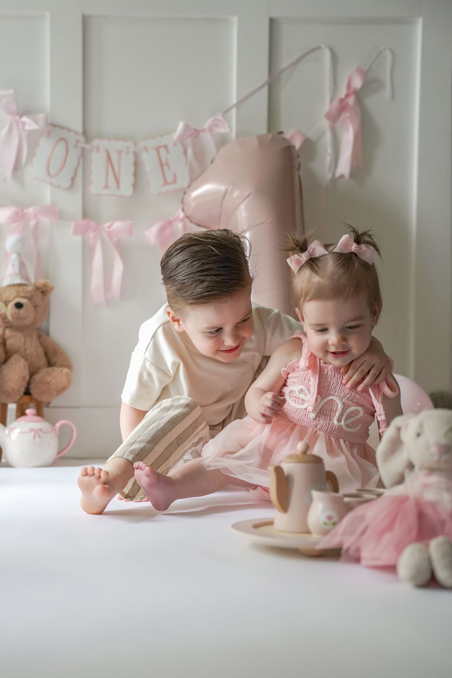 Children enjoying a pink-themed tea party setting with stuffed animals, decorative banners and pastel decor.